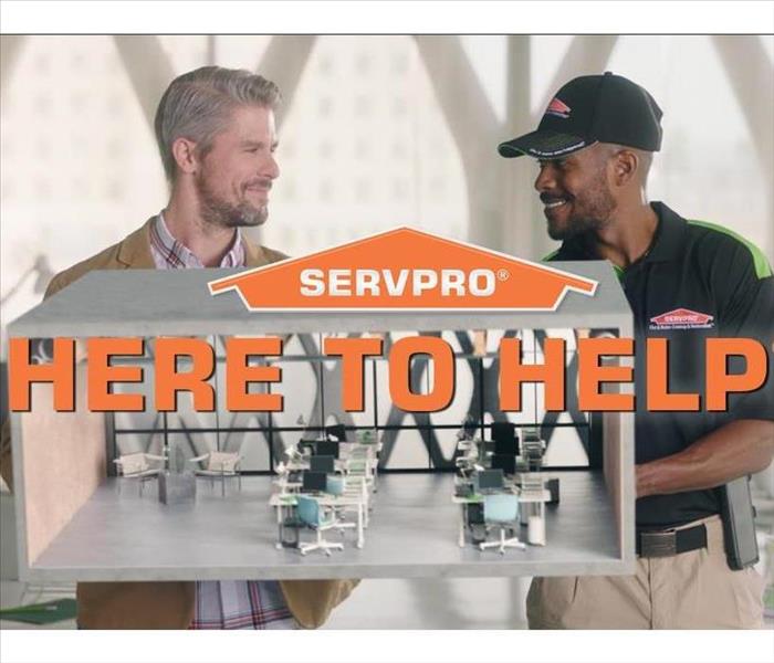 SERVPRO male employee with customer in office space or classroom with text that says Here to help