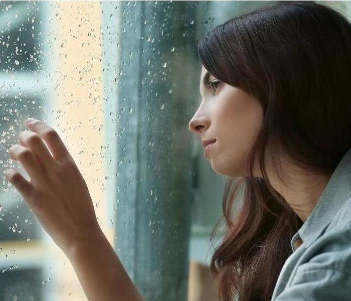 Woman looking out rain covered window at flood